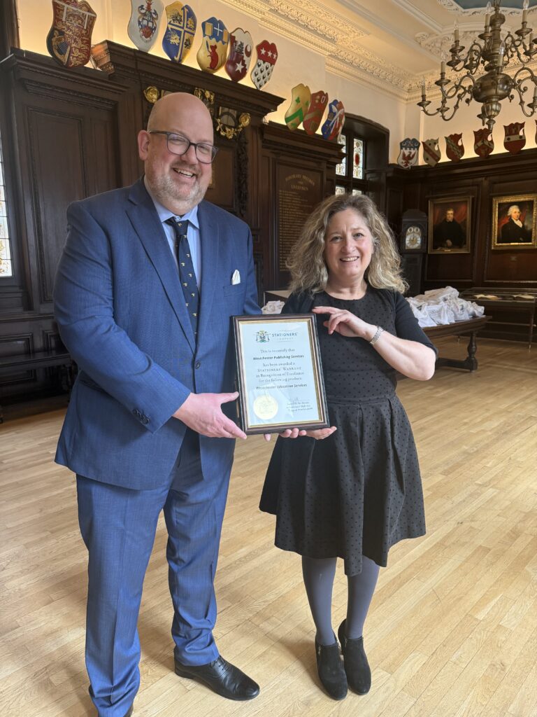 Main in a suit and woman in a dress holding a framed copy of a 2026 Stationers Company warrant.